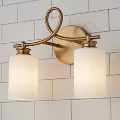 two light bathroom fixture with white glass shades on the bottom and gold finish, against a white brick wall