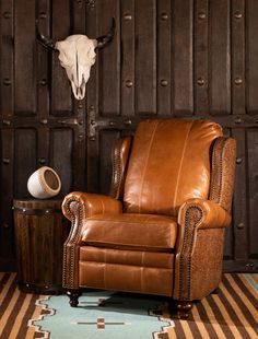 a brown leather recliner chair sitting in front of a cow skull on the wall