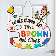 a welcome sign hanging on a door with paintbrushes and crayons painted on it