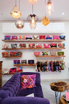 a purple couch sitting in front of a wooden shelf filled with purses and bags