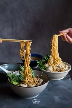 someone holding chopsticks over some noodles in two bowls with another bowl on the side