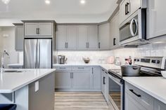 a kitchen with gray cabinets and white counter tops, stainless steel appliances and an island