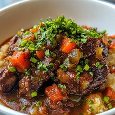 a white bowl filled with meat and vegetables on top of mashed potatoes, garnished with parsley