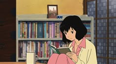 a woman sitting in front of a book shelf holding a book and looking at it