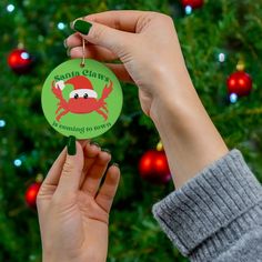 someone holding up a christmas ornament in front of a tree