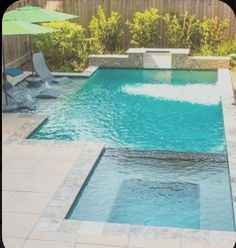 an empty pool with chairs and umbrellas in the back yard, next to a wooden fence