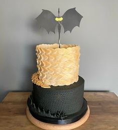 a black and white cake with a bat decoration on top, sitting on a wooden table