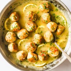 a bowl filled with meatballs covered in gravy and garnished with lemon wedges