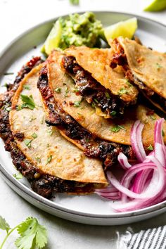 some tacos are on a plate with onions and guacamole next to it