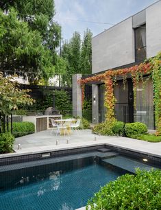 an outdoor swimming pool surrounded by greenery and shrubs, with a dining table in the middle