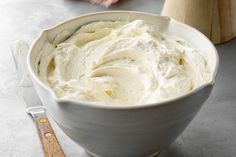 a white bowl filled with whipped cream next to a wooden utensil on top of a table