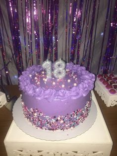 a birthday cake with purple frosting and flowers on top, surrounded by confetti