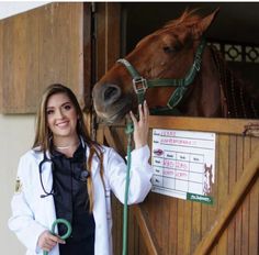 a woman standing next to a brown horse in a stable with her hand on the bridle