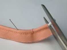 a pair of scissors cutting through a pink piece of fabric with two pins in it