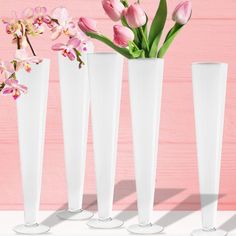 three tall white vases with pink flowers in them on a table against a pink background