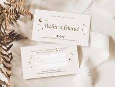 two white business cards sitting on top of each other next to some plants and leaves