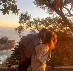 a man and woman kissing on top of a hill near the ocean in front of trees