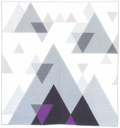 a quilted wall hanging with grey and purple triangles in the middle, on a white background