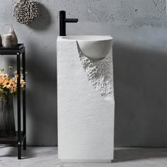 a white pedestal sink sitting next to a vase with flowers in it on a table