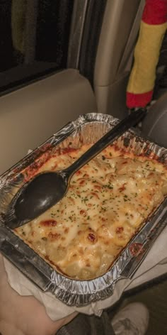 a person holding a pan of macaroni and cheese with a spoon in it