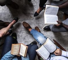 several people are sitting in a circle reading books and looking down at the floor with their legs crossed