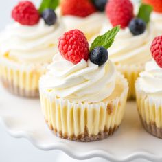 some cupcakes with white frosting and berries on top are sitting on a plate