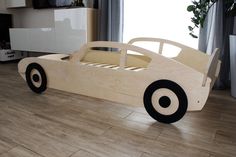 a wooden car bed sitting on top of a hard wood floor next to a window