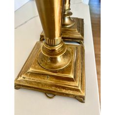 two brass candlesticks sitting on top of a white table next to each other