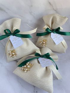 three small bags with green ribbon and gold brooches on them sitting on a marble surface