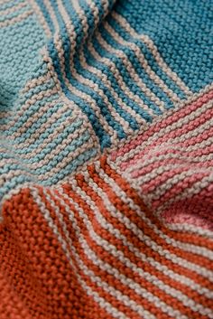 an orange, blue and white knitted blanket laying on top of each other