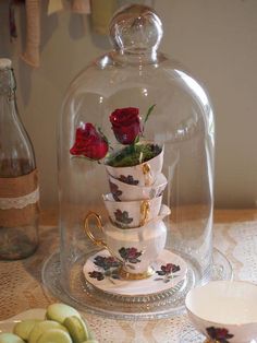 a glass cloche with roses in it sitting on top of a table next to plates and cups