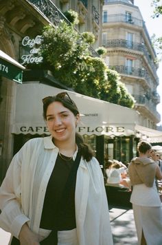 a woman standing in front of a cafe on the street with people walking around her