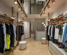 a clothing store with clothes on racks and lights hanging from the ceiling above it's wooden flooring