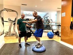 two men in a gym doing exercises on exercise balls with an exercise machine behind them