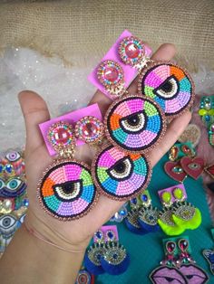 a person is holding several pairs of colorful earring sets in their hand, with other jewelry on the table