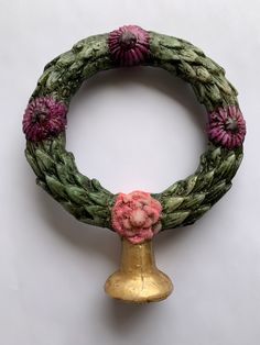 a wreath with pink flowers on it and a gold bell in the middle, against a white background