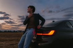 a man leaning on the trunk of a car in a field at sunset or dawn