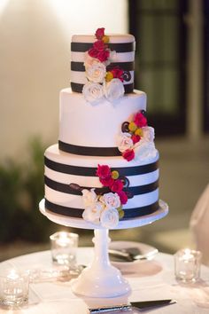 a three tiered cake with black and white stripes, flowers on the top is sitting on a table