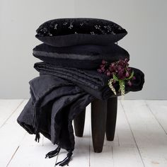 a stack of black pillows sitting on top of a wooden table next to a vase filled with flowers