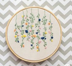 an embroidered flower pattern on a white and gray chevron wallpaper with a wooden hoop