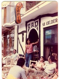 a group of people sitting at tables in front of a building with a sign on it