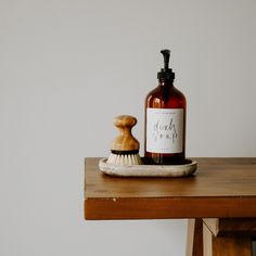 a bottle of soap sitting on top of a wooden table next to a scrub brush