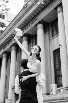 a man holding a woman on his back in front of an old building with columns