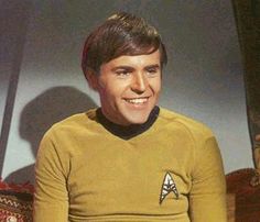 a man in a star trek uniform sitting on a couch with his hand on his hips