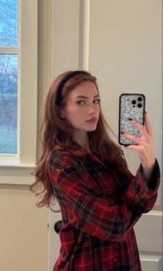 a woman taking a selfie with her cell phone in front of the camera while wearing a red and black flannel shirt