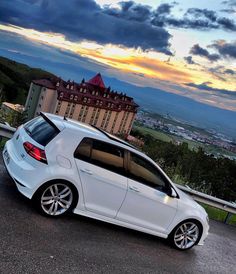 a white car parked in front of a building on top of a hill with a sunset behind it