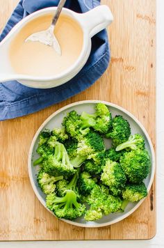 broccoli florets in a white bowl on a wooden cutting board next to a spoon