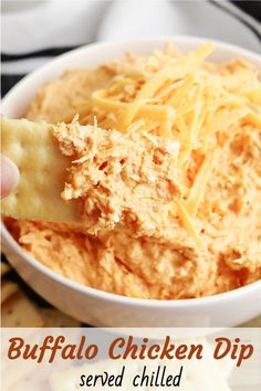 a cracker being dipped with cheese in a white bowl