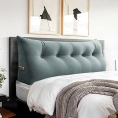 a bed with a blue tufted headboard next to two framed pictures on the wall