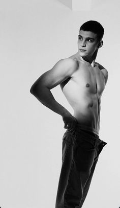 a shirtless young man poses for a black and white photo with his hands on his hips